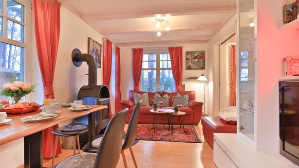 A cozy living room with a fireplace, a dining area with a table set for two, and a sofa with decorative pillows. - Landhaus Victoria, Schwan (Ostseebad Boltenhagen)