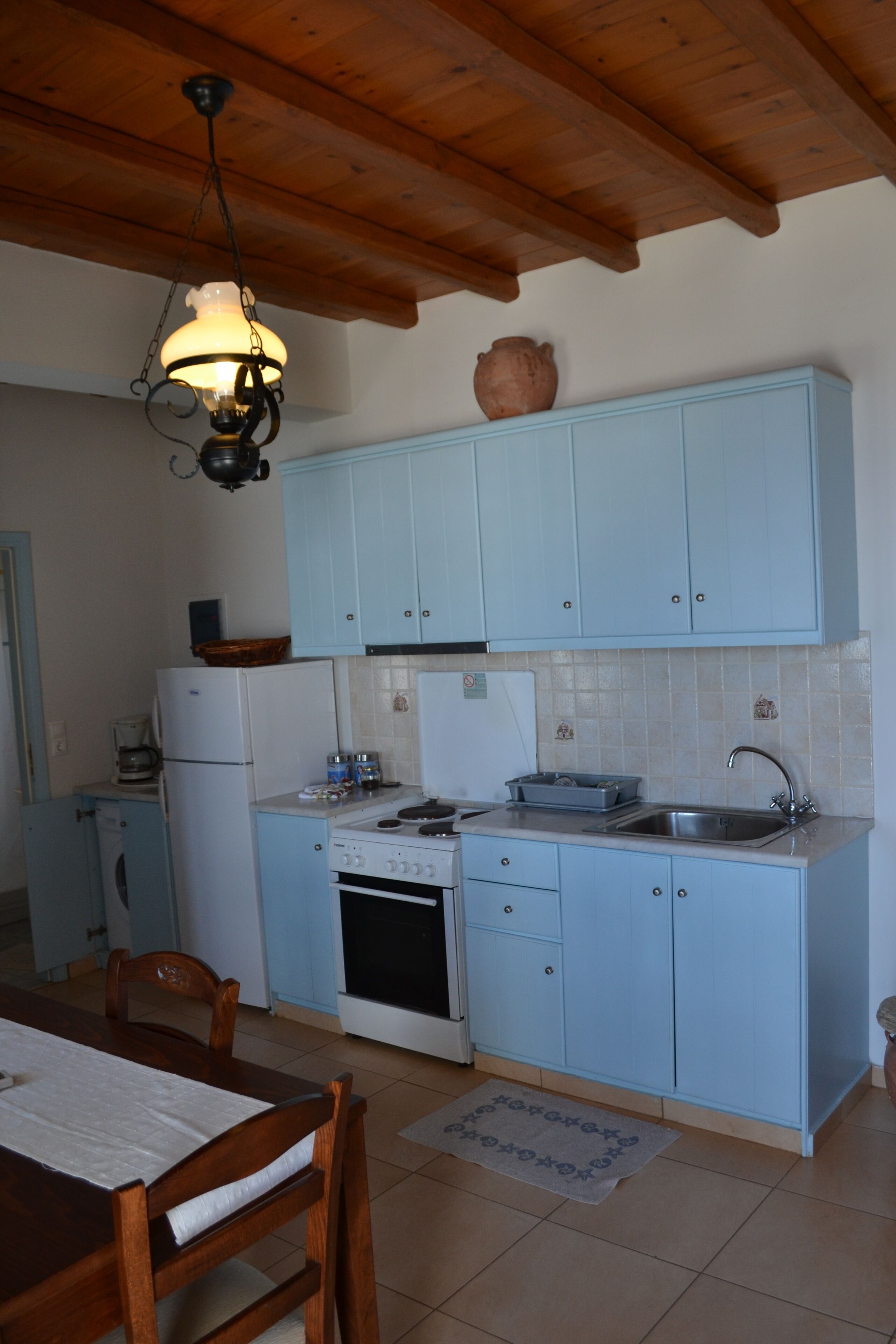 Una cocina con armarios azul claro, techo de madera, lámpara colgante, estufa y refrigerador.