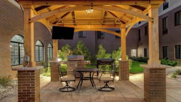 An outdoor patio with a wooden pergola, brick walls, and a flat-screen TV mounted on the wall.