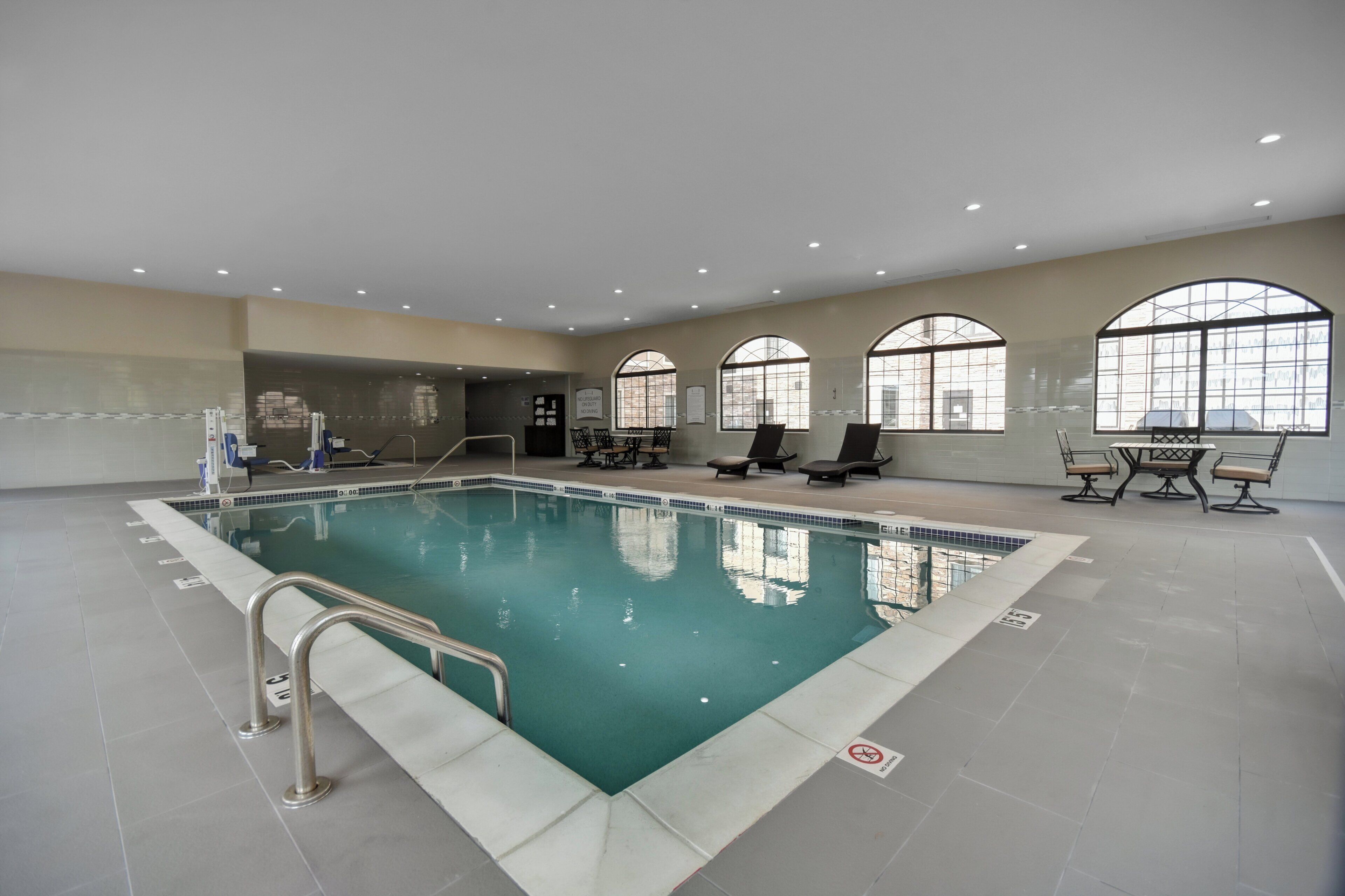Una piscina interior con agua cristalina, rodeada de sillas de descanso y un suelo de baldosas.