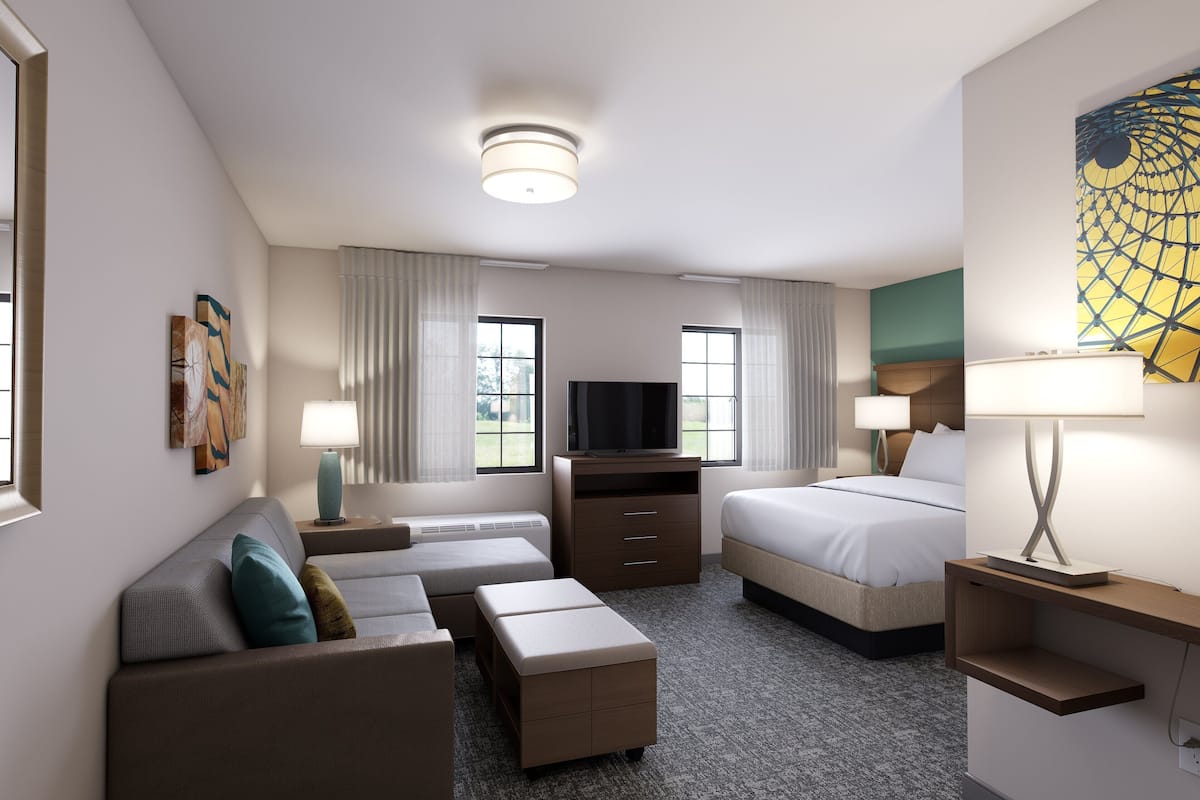 Ein modernes Hotelzimmer mit einer Couch, einem Bett, einem Fernseher und einem Schreibtisch mit einer Lampe.