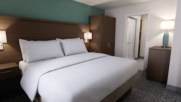 Habitación de hotel con una cama grande, cabecero de madera, dos lámparas de noche, una mesita de noche, un armario y la puerta de un baño.