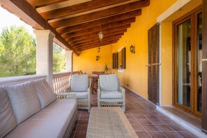 Une terrasse couverte, meublée de meubles en osier, avec un plafond en bois et un mur jaune.