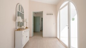 A hallway with a white console table, lamps, and a mirror. There is a door leading to another room.