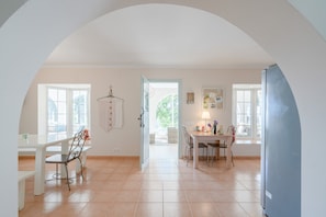 A kitchen with a dining area, a refrigerator, and a view through an open door. - Stunning Rural Home “Finca Colica” with Sea View, Mountain View (Cómpeta)