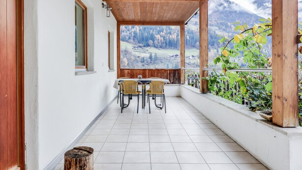 Un balcon abrité avec une table et des chaises, une vue sur un paysage montagneux et un plafond en bois.