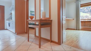 Eine moderne Küche mit weißen Schränken, einem Holztisch mit Spiegel und Blick auf einen Wald durch ein Fenster.
