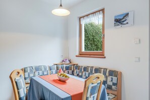 A dining area with a table, chairs, a bowl of fruit, a window with a view, and a wall-mounted calendar.
