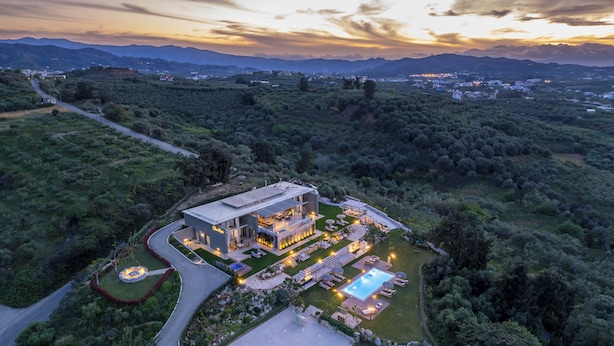 Une villa moderne dotée d’une piscine, entourée d’une végétation luxuriante et bordée d’un chemin sinueux.