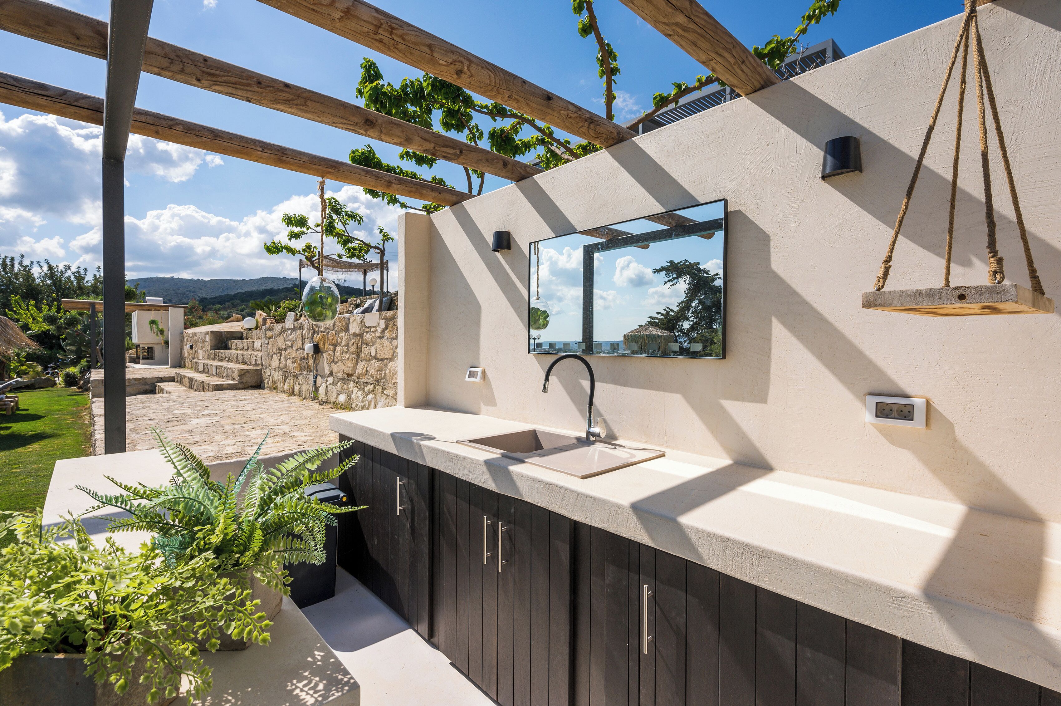 An outdoor kitchen with a sink, a hanging swing, and a stone wall in the background.