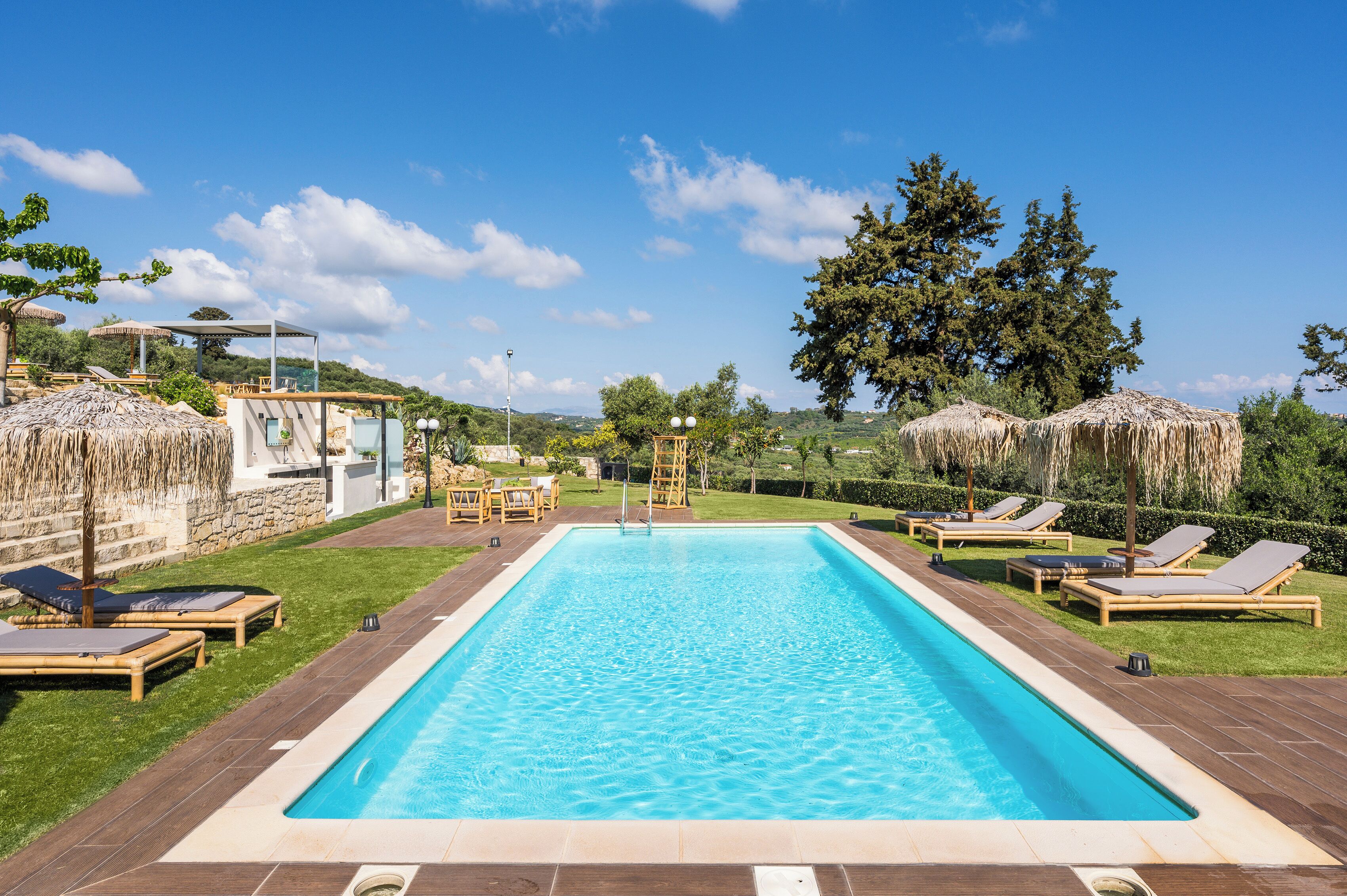 Una piscina rectangular con superficie de agua azul cristalina, rodeada de un suelo de madera y sillas de descanso.