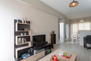A modern living room with a flat-screen TV, wooden shelving, a coffee table, and a dining area in the background. - Central Luxury Apartment (Rethymno)