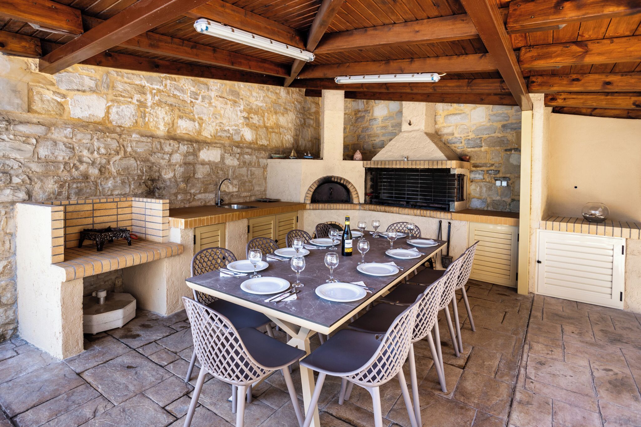 An outdoor kitchen with stone walls, a brick oven, and a dining table set for six.