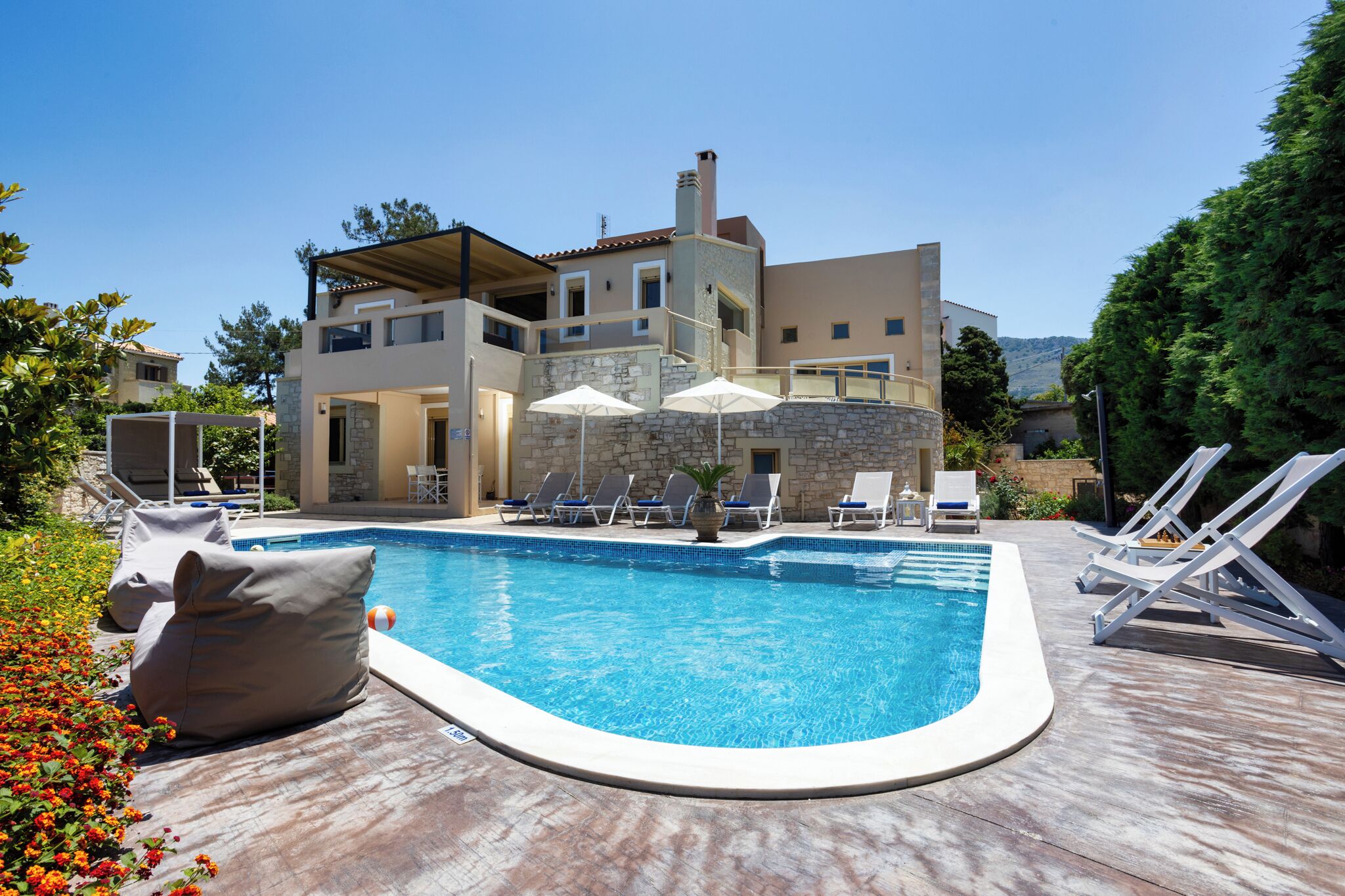 Ein modernes, zweistöckiges Gebäude mit Swimmingpool, Liegestühlen und Sonnenschirmen.