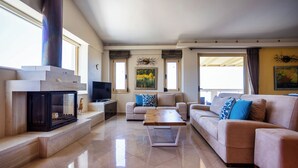 A spacious living room with a fireplace, a sofa set, and a television. - Palladio Luxury Villa With Amazing View (Rethymno)
