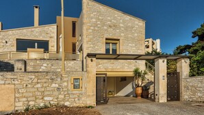 A modern stone building with a stone facade, a covered entrance, and a small balcony. - Palladio Luxury Villa With Amazing View (Rethymno)