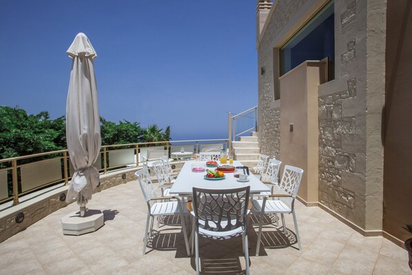 Enjoy meals al fresco with a view of the sea from this outdoor dining area, featuring a table for four and comfortable seating.