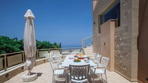 An outdoor dining area with a table and chairs, a statue, and a view of the sea. - Palladio Luxury Villa With Amazing View (Rethymno)