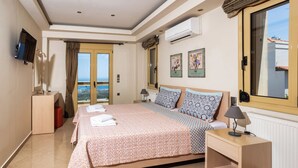 A hotel room with a large bed, a TV, an air conditioner, a window with curtains, and a view of the sea. - Palladio Luxury Villa With Amazing View (Rethymno)