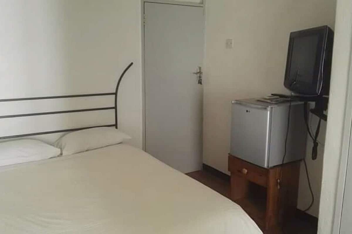 A simple room with a bed, a door, and a small TV on a stand.