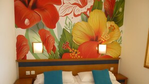Ein Hotelzimmer mit einer großen Blumenmalerei an der Wand, einem hölzernen Kopfteil, zwei Nachttischen und einem Bett mit weißer Bettwäsche und blauen Kissen.