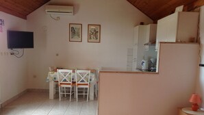 Una habitació petita i acollidora amb un llit, una taula de menjador amb caires, una zona de cuina i un televisor penjat.