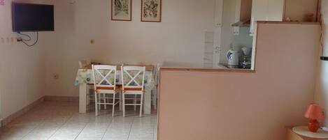 Quarto pequeno e aconchegante com uma cama, uma mesa de jantar com cadeiras, um espaço de cozinha e uma TV montada na parede.