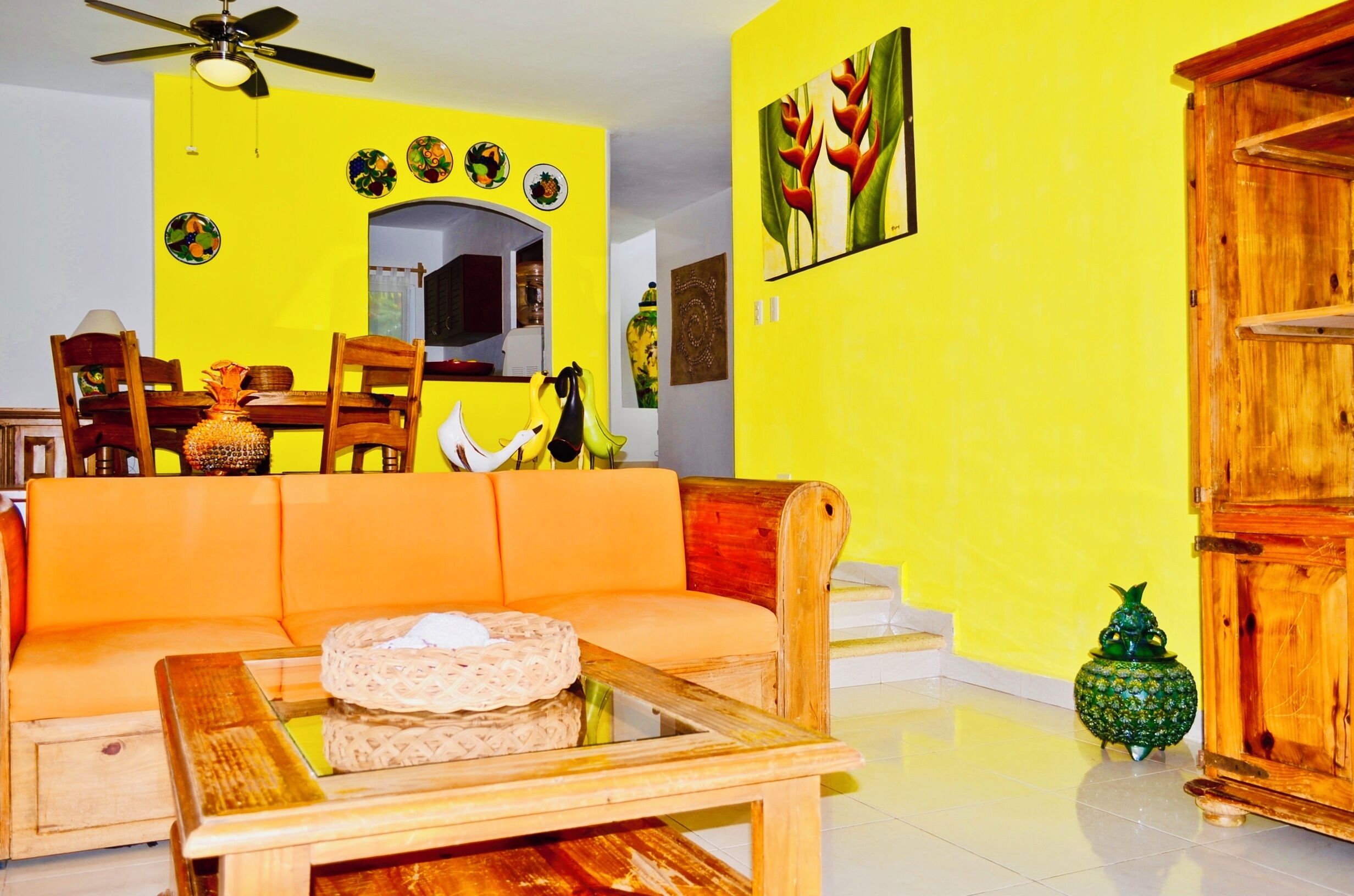 A living room with a yellow wall, a wooden sofa, a glass coffee table, and a wooden cabinet.
