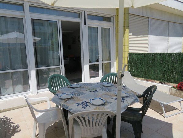 An outdoor patio with a table set for four, surrounded by white plastic chairs.