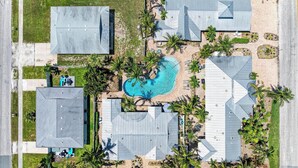 Vista aérea de un complejo turístico con varias edificaciones, una piscina y palmeras.