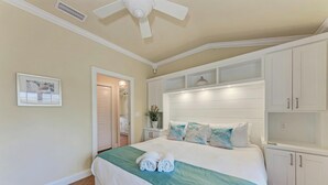 Una habitación de hotel con cama, armarios blancos, un ventilador de techo y un cuadro enmarcado en la pared.