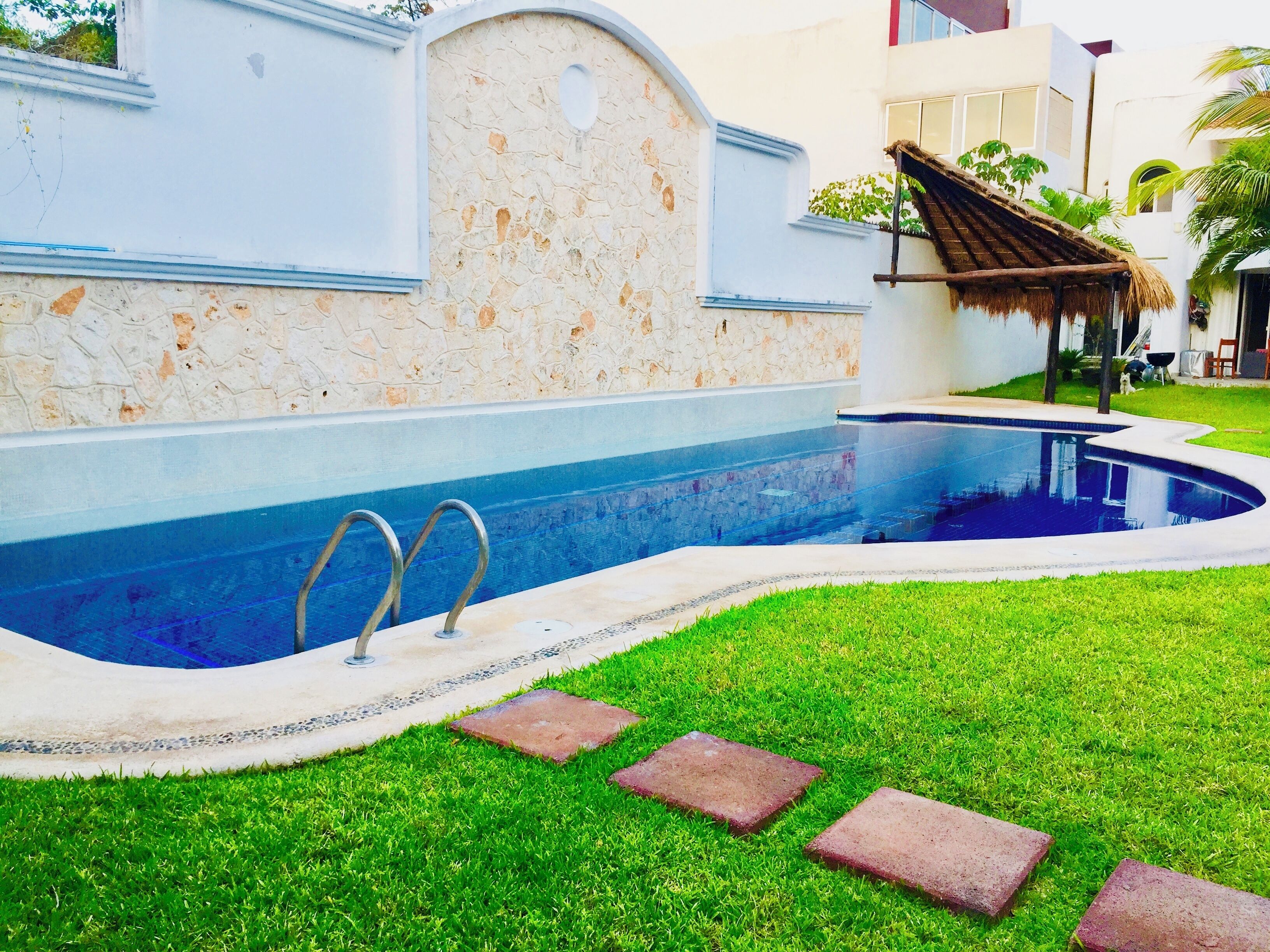 A swimming pool with a stone wall and a thatched roof structure.