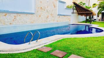 A swimming pool with a stone wall and a thatched roof structure.