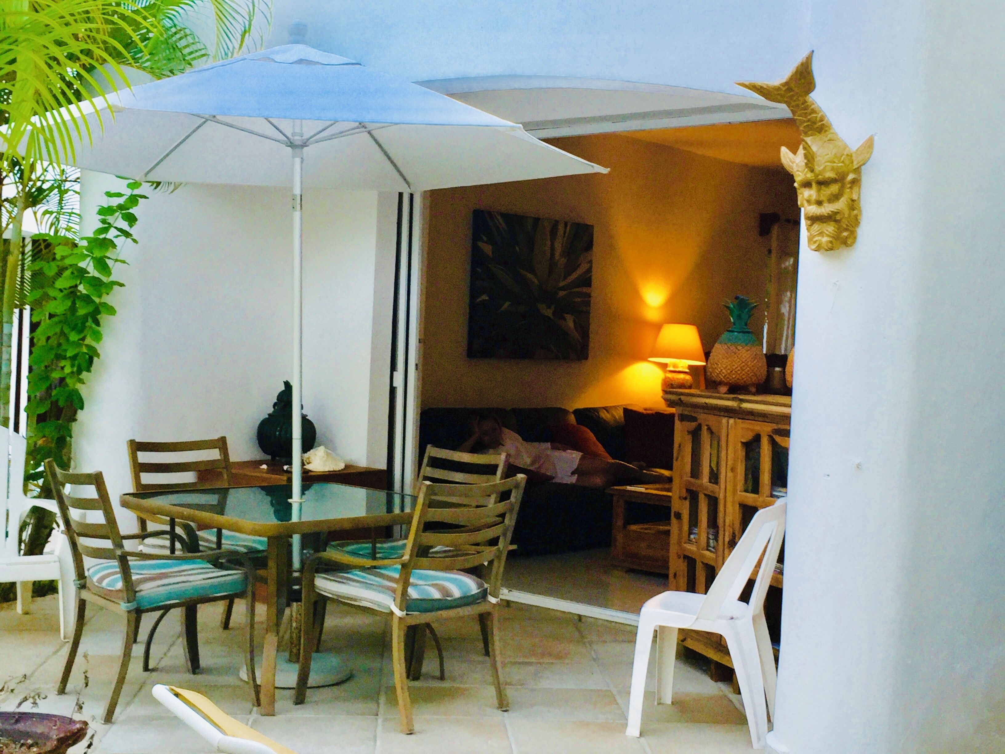 Un espace de restauration en plein air avec une table et des chaises, un parasol blanc et une sculpture fixée au mur.