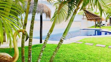 Un área de piscina con una estructura de techo de paja, palmeras y un flamenco.
