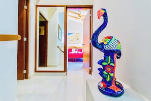 A hallway with a wooden door leading to a room with a bed and a ceiling fan. A colorful sculpture is placed on the floor. - Room-executive Budget Room With Swimming (Playa del Carmen)