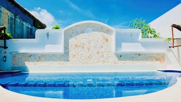Una piscina con un muro de piedra y un cielo azul despejado.