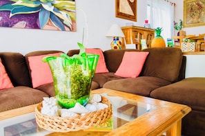 A living room with a sofa, a glass coffee table, a wicker basket, and a green vase with plants.