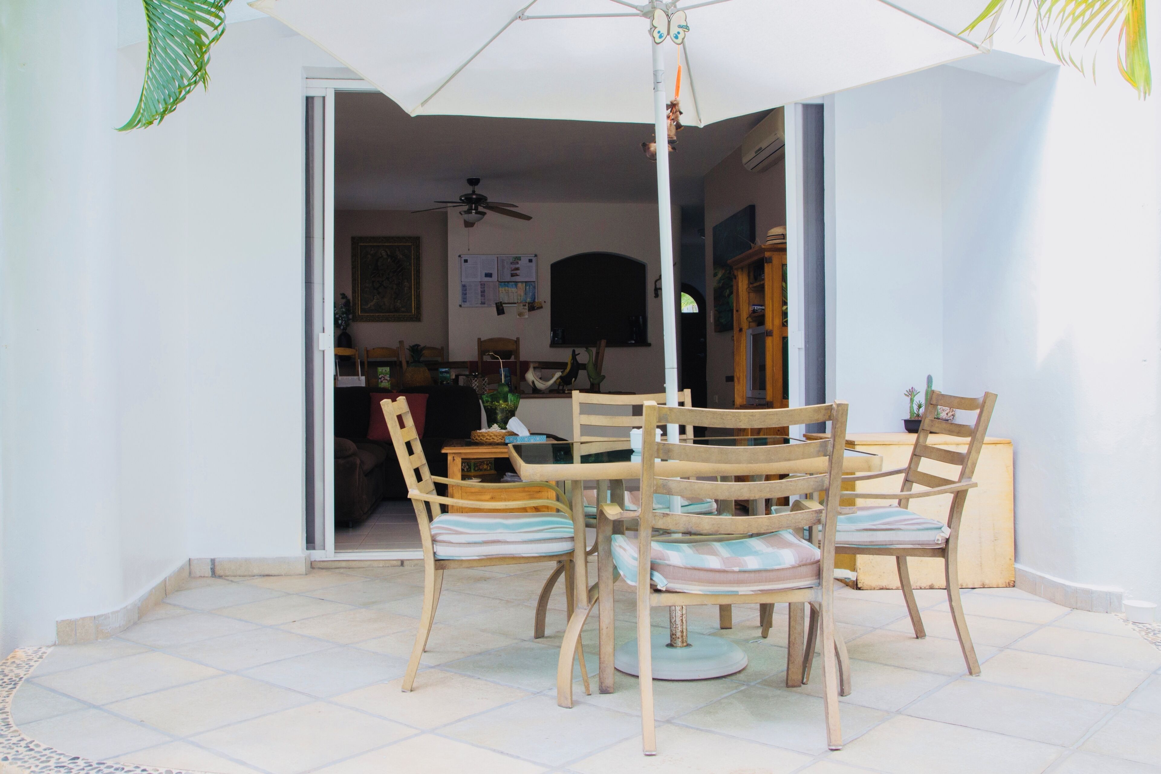Un área de comedor al aire libre con una mesa, sillas, una sombrilla y vistas al interior de la casa.