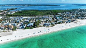 An aerial view of a coastal town with a beach, clear blue waters, and a mix of residential and commercial buildings.