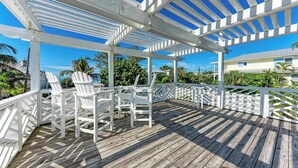 A wooden deck with white chairs and a pergola structure.