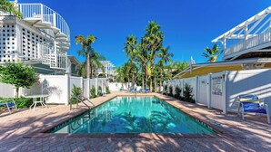 A pool area with a clear blue pool, lounge chairs, and palm trees.