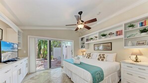 A bedroom with a bed, a ceiling fan, a TV, and a sliding glass door leading to an outdoor area.