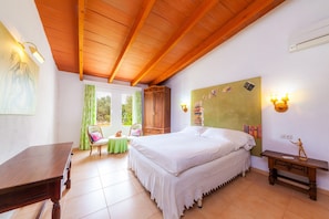 A bedroom with a wooden ceiling, a bed with white bedding, a green wall with decorations, a small table with chairs, and a wooden nightstand. - Villa "Can Me Sents" with Large Garden and Pool (pollensa)