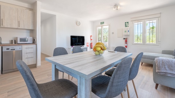 Una cocina moderna con lavavajillas, microondas y un comedor con mesa de madera y sillas grises.
