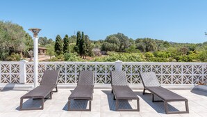 Una terraza en la azotea con tres tumbonas, una lámpara decorativa y una valla de celosía blanca.