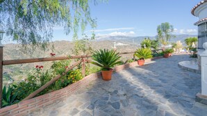 A stone-paved patio with potted plants and a wooden fence overlooking a mountainous landscape. - Peaceful Home Cortijo La Rijana with Pool, Terrific Views, Terrace, Wi-Fi (Sayalonga)