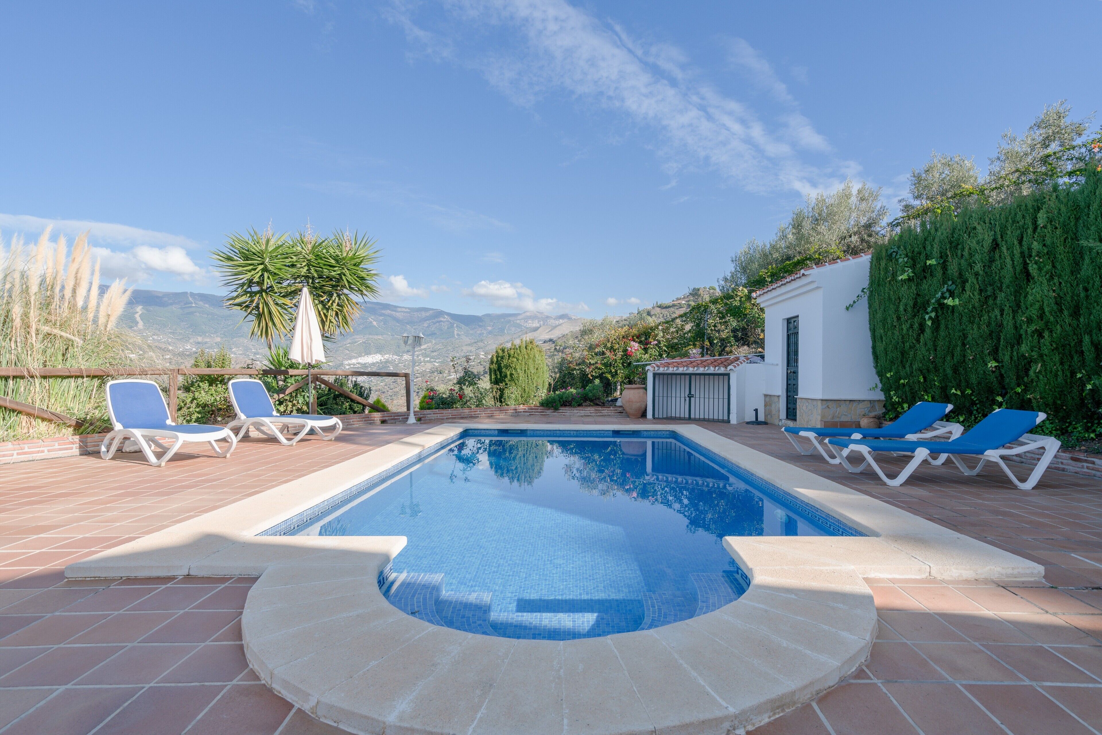 Une piscine avec des chaises longues, un bâtiment blanc et une chaîne de montagnes en arrière-plan.