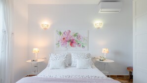 A bedroom with a bed, two bedside tables, a wall-mounted air conditioner, and a floral painting. - Peaceful Home Cortijo La Rijana with Pool, Terrific Views, Terrace, Wi-Fi (Sayalonga)