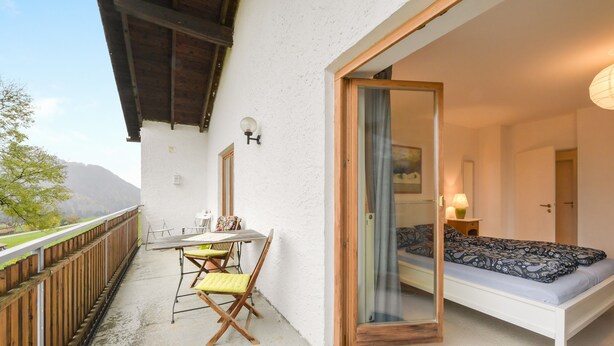 Un balcón con mesa y sillas, una cama con ropa de cama estampada y vistas a la montaña.